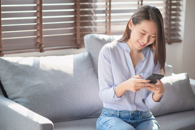 Young man using mobile phone while sitting on sofa at home