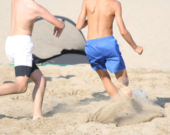 Low section of men playing on sand at beach