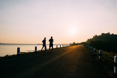 Silhouette people running on road against clear sky during sunset