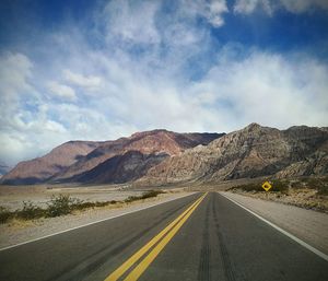 Empty road by mountains against sky