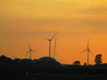 Silhouette wind turbines on field against orange sky