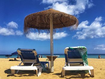 Deck chairs on beach against sky