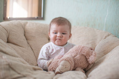 Baby girl with teddy bear on sofa at home