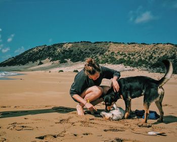 Woman crouching by playful dogs at beach