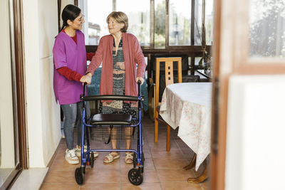 Smiling caregiver helping senior woman to walk with mobility walker at home