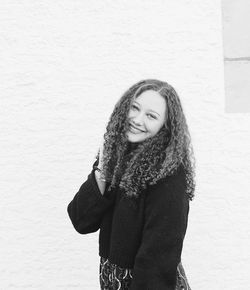 Portrait of smiling young woman with curly hair standing against wall