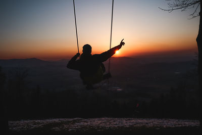 Silhouette man with arms raised against sky during sunset