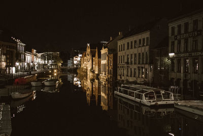 Sailboats moored on canal by illuminated buildings in city at night