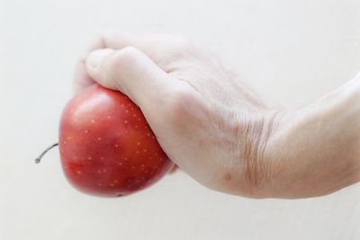 Cropped hand of person holding fruit against white background