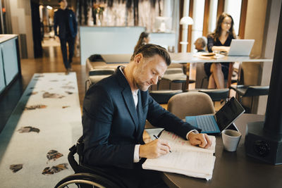 Disabled businessman writing in book at table in cafeteria