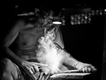 Shirtless manual worker smoking cigarette while working at night