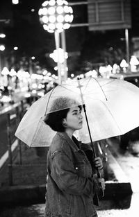 Young woman with umbrella in city at night during rain