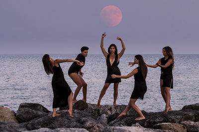 Fashion models posing on rocks by sea against sky