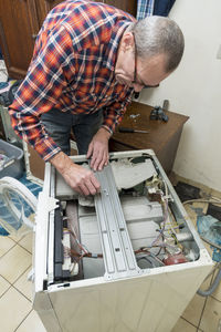 Middle aged man repairing broken washing machine with tools, household chores