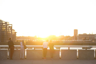 Rear view of young couples standing on bridge during sunset