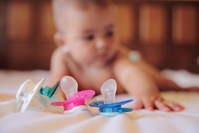 Close-up of shirtless baby girl lying by pacifiers in crib
