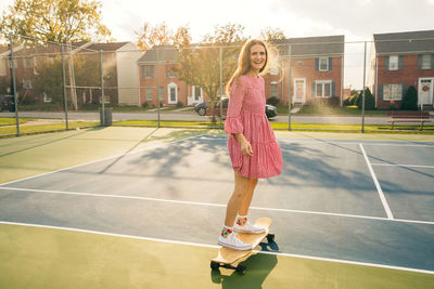Smiling girl learning how to skateboard on a tennis court with sunlight on her hair
