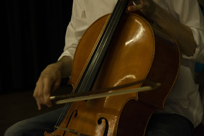 Midsection of man playing double bass against black background