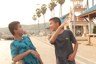 Boy gesturing to friend while standing at pier against sky