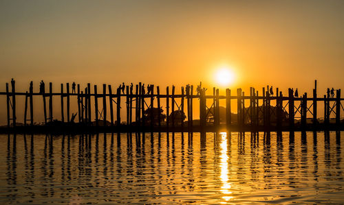 Silhouette people on sea against sky during sunset