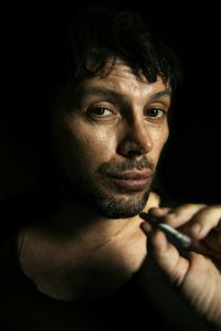 Portrait of man holding cigarette against black background