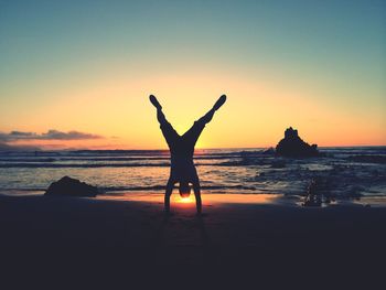 Silhouette of woman jumping on beach at sunset