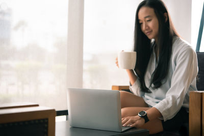 Young woman using phone while sitting on table