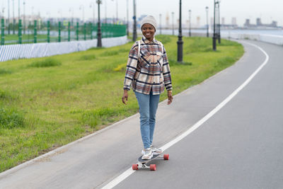 Happy young afro woman skating on longboard smiling relax with skateboard outdoor in city space