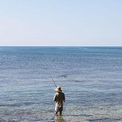 Rear view of man fishing in sea against clear sky