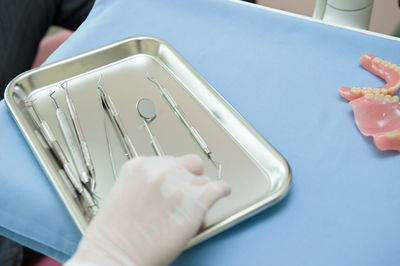 Cropped hand of dentist holding dental equipment in tray on table