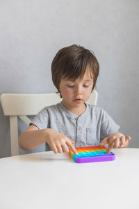 Adorable boy is playing at home with a new trendy silicone pop it toy. 