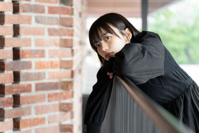 Portrait of young woman standing against brick wall