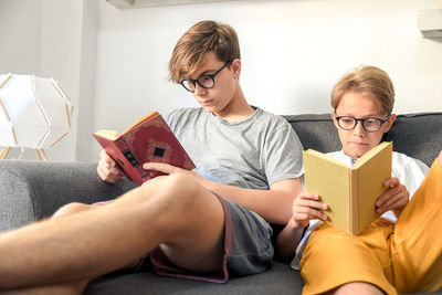 Brothers reading book on sofa at home