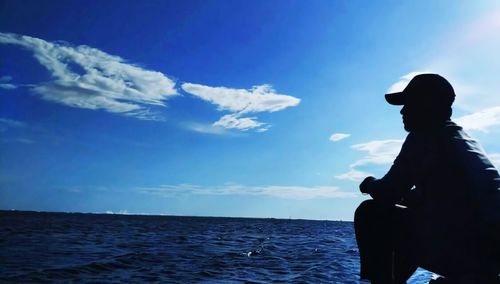 Silhouette man standing by sea against blue sky