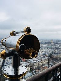 Close-up of coin-operated binoculars overlooking cityscape against sky