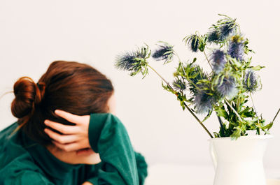 Rear view of woman by flower vase against white background