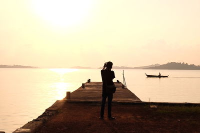 Rear view of silhouette man standing on pier over sea against sky during sunset