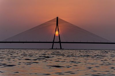 Silhouette bridge over sea against orange sky