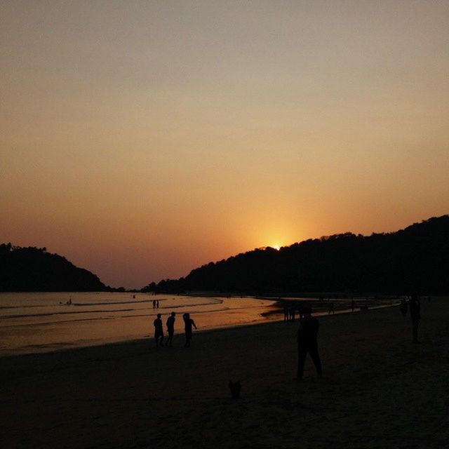 sunset, beach, sea, silhouette, water, large group of people, copy space, scenics, clear sky, leisure activity, shore, beauty in nature, mountain, tranquil scene, vacations, lifestyles, tranquility, men, nature