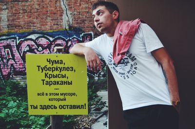 Young man looking away while standing by sign board