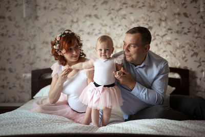 Gentle parents with a daughter on the bed in a real room, the concept of parenthood and affection
