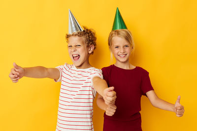 Happy siblings with party hats gesturing thumbs up against yellow background