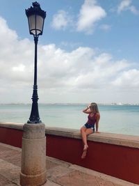 Woman sitting on retaining wall against sea