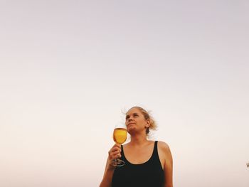 Young woman holding wineglass against clear sky