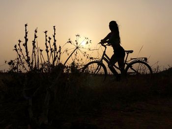 Silhouette woman with bicycle on land against clear sky during sunset
