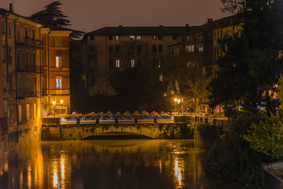 Illuminated bridge over canal by buildings in city at night