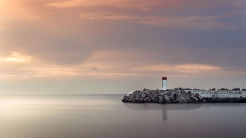 Lighthouse by sea against sky during sunset