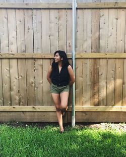 Happy woman looking away while leaning against wooden fence