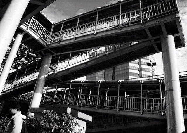 architecture, built structure, railing, low angle view, staircase, steps, building exterior, steps and staircases, architectural column, bridge - man made structure, building, connection, balcony, day, arch, metal, outdoors, sunlight, city, footbridge