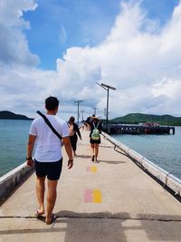 People walking on bridge over sea against mountain